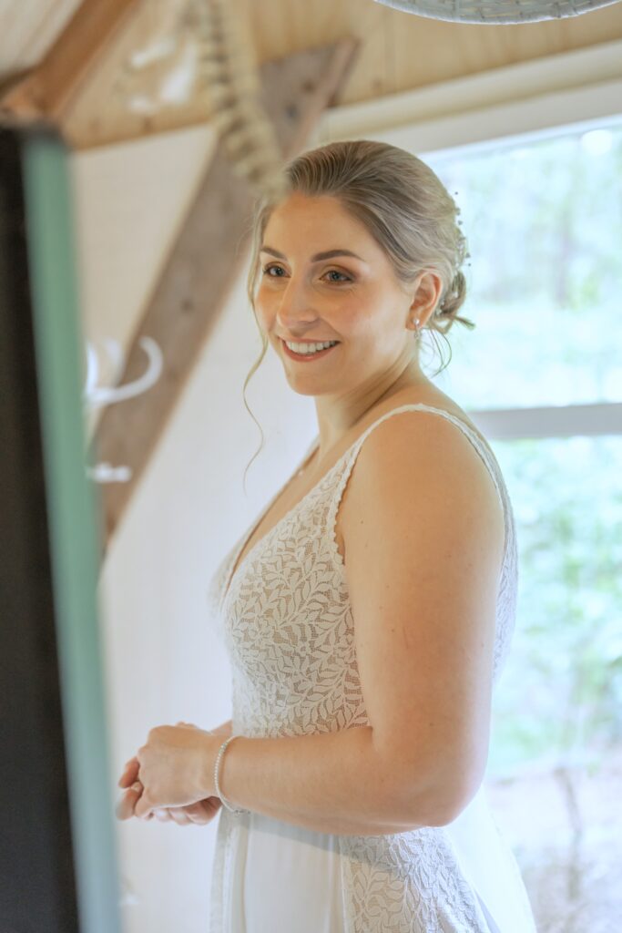 Bruid bewondert zichzelf met klassieke opgestoken haarstijl en natuurlijke make-up look.