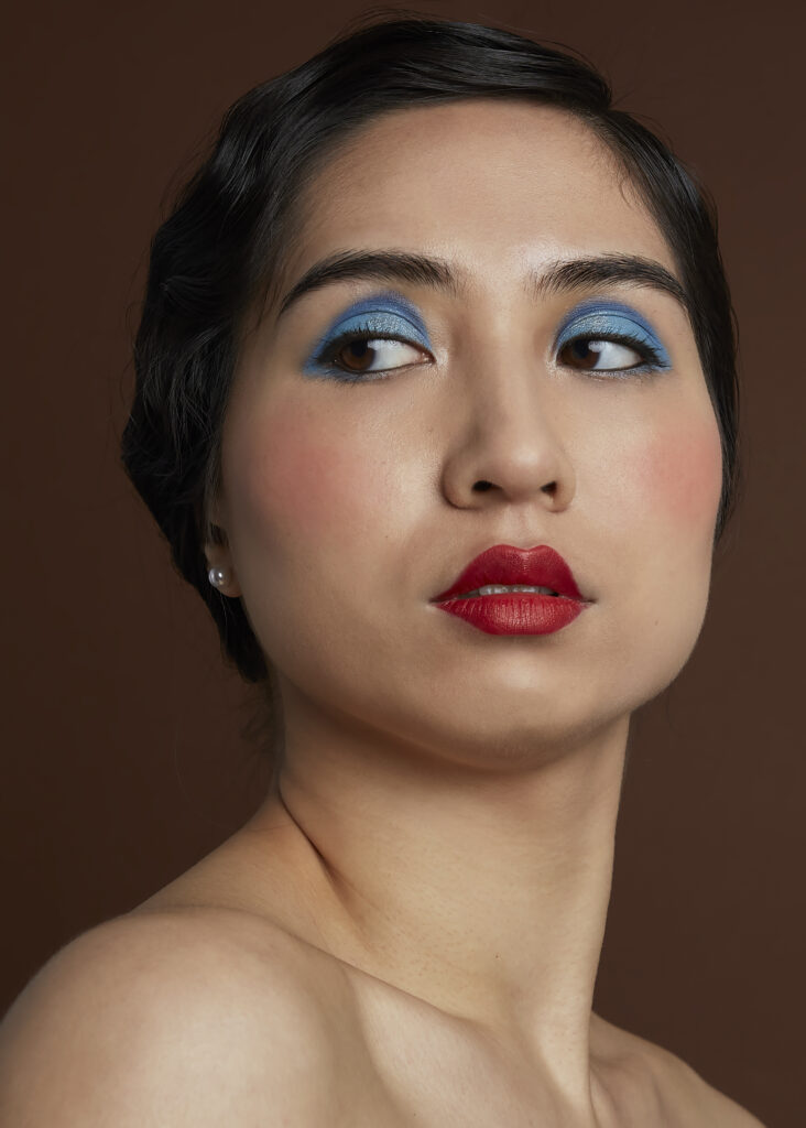 Model met jaren 20 make-up look, blauwe oogschaduw en rode lippenstift, gecombineerd met een vintage haarstijl.
